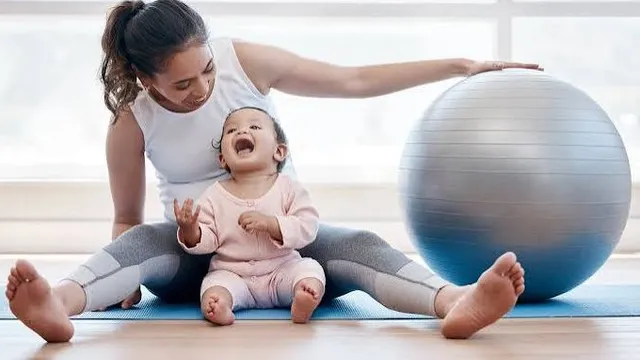 A mother and her laughing baby on a mat beside an exercise ball