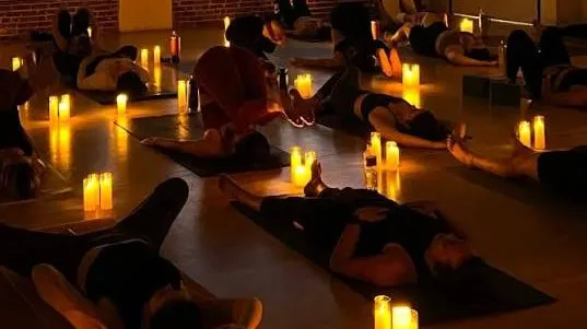 Students resting on their mats in a dark room lit by candles