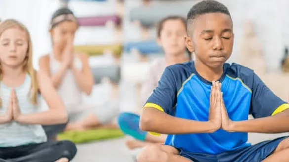 Children seated on mats with their palms together and their eyes closed
