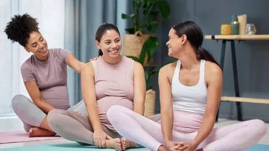 Three women seated on mats and talking, one of them pregnant