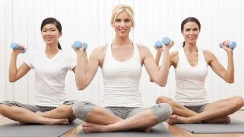 Three women seated cross-legged, each holding a pair of small blue hand weights
